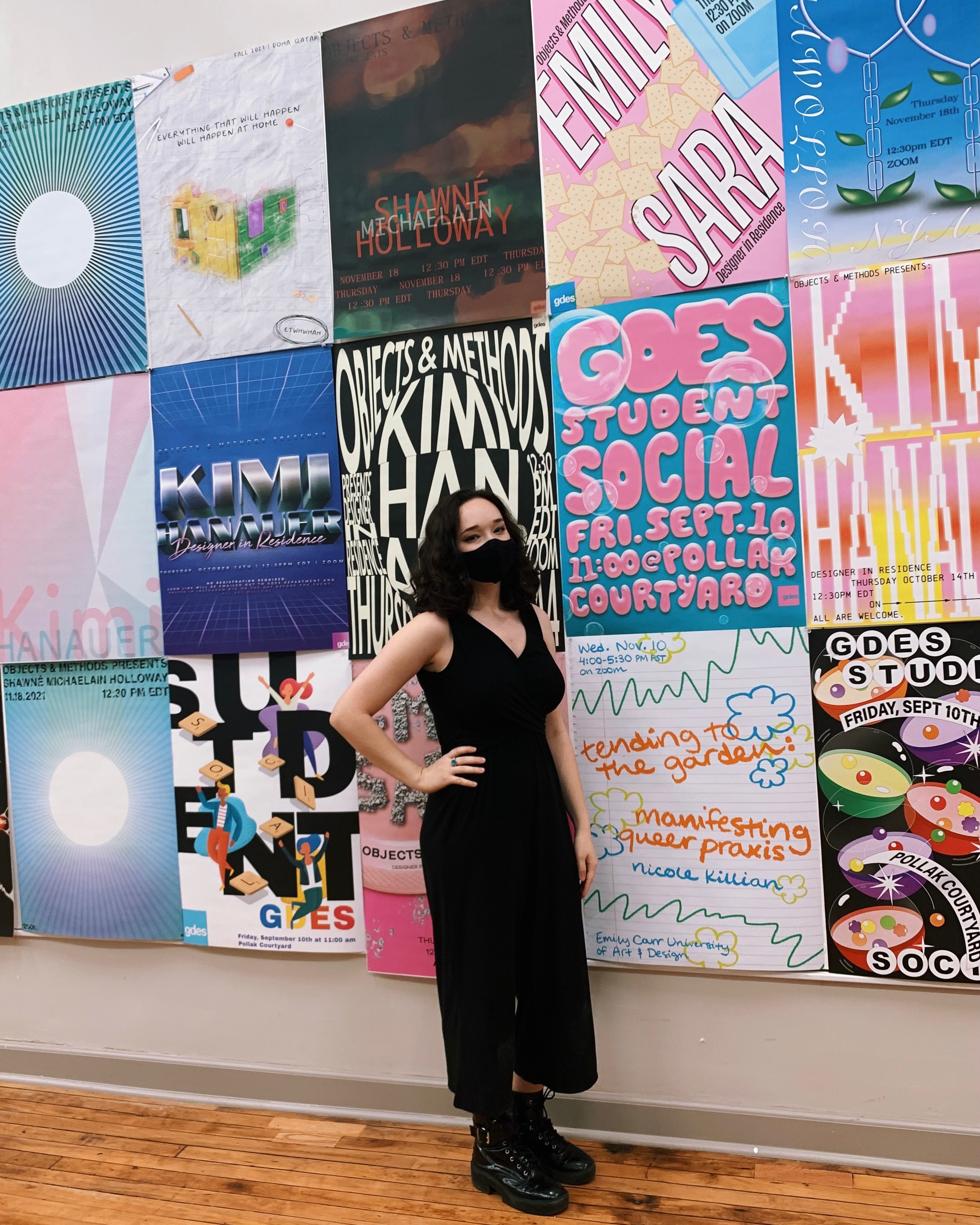 elora, dressed in all black, standing in front of a wall of posters